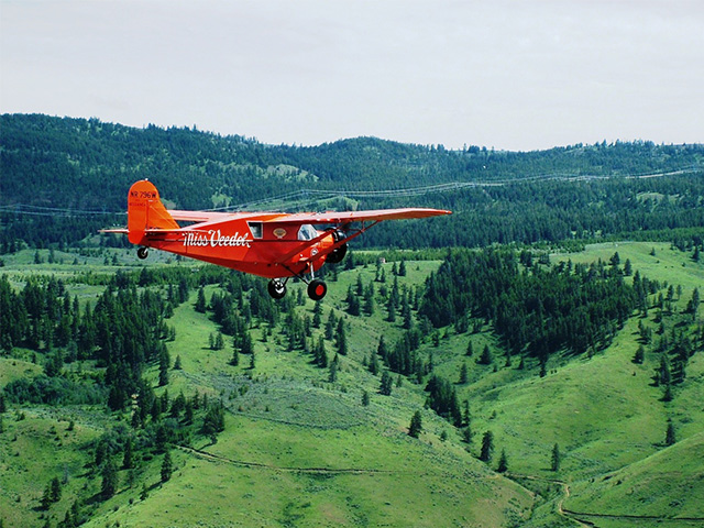 Image of a red airplane flying over a green landscape